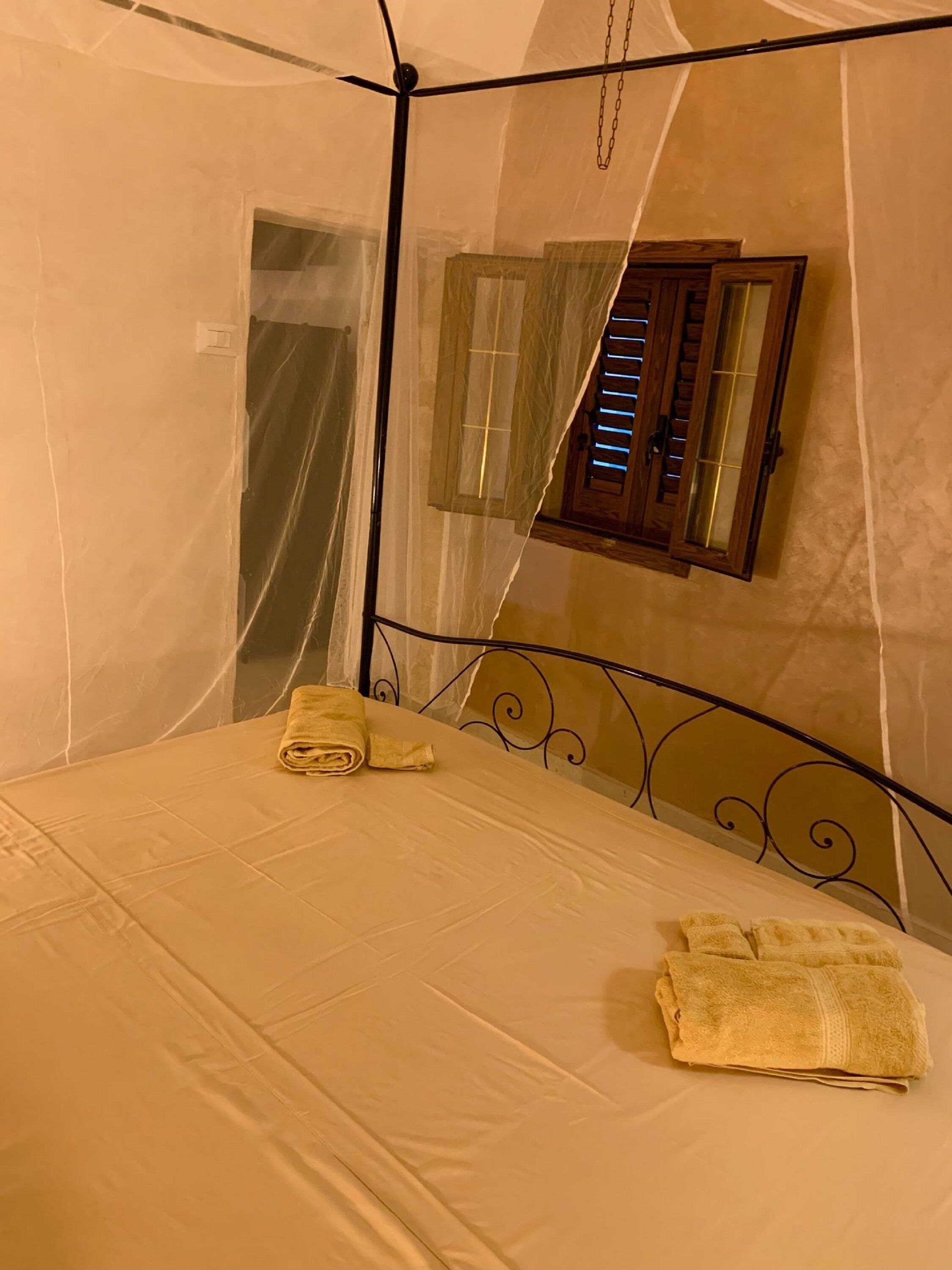A single bed with a mosquito net, a wooden headboard, and a window with blinds.