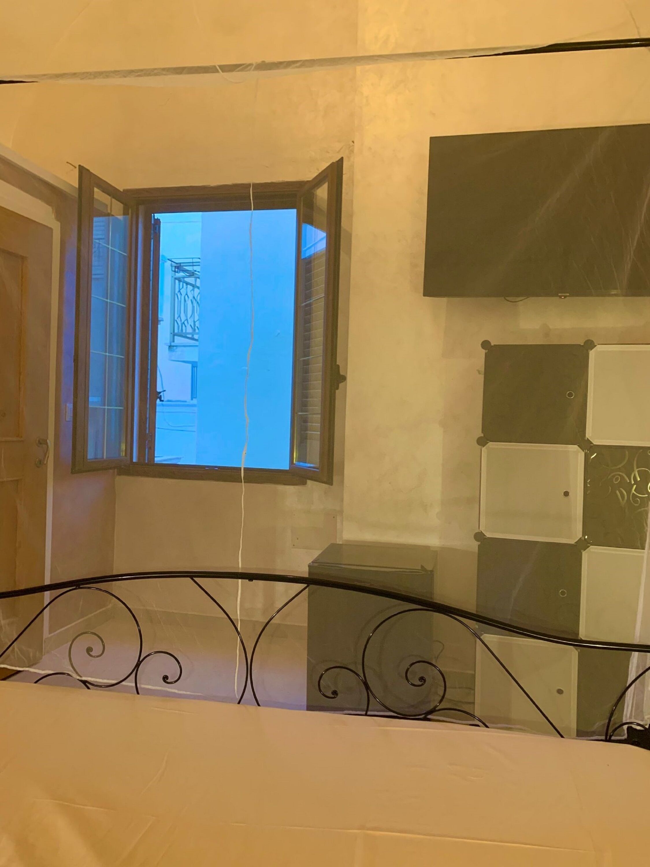 Une pièce avec un lit, une fenêtre avec des rideaux, un téléviseur fixé au mur et une porte.