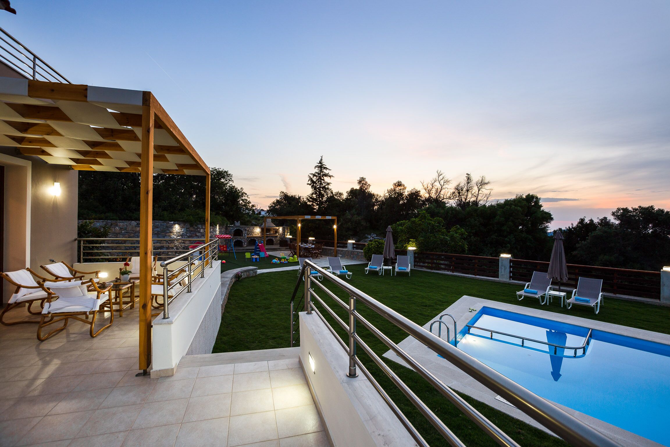 Une piscine dotée d’une terrasse en bois et de chaises longues, entourée d’une pelouse bien entretenue et d’un patio abrité.