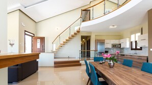 A spacious living area with a wooden dining table, blue chairs, and a staircase leading to an upper level. - Anatoli Villa, a Retreat with Private Pool & BBQ (Rethymno)