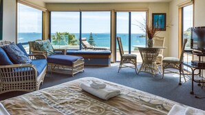 Una habitación con cama, dos sillones de mimbre, una mesita, televisor y ventanas amplias con vista al océano.