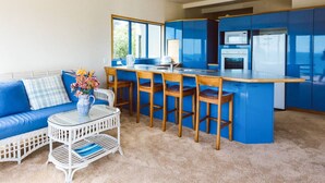 Una cocina moderna con armarios azules, una isla central y una zona de estar con sofá y una mesa de mimbre blanco.