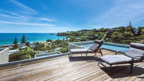 Terraza de madera con dos sillones de descanso que dan a una piscina y vistas al mar.