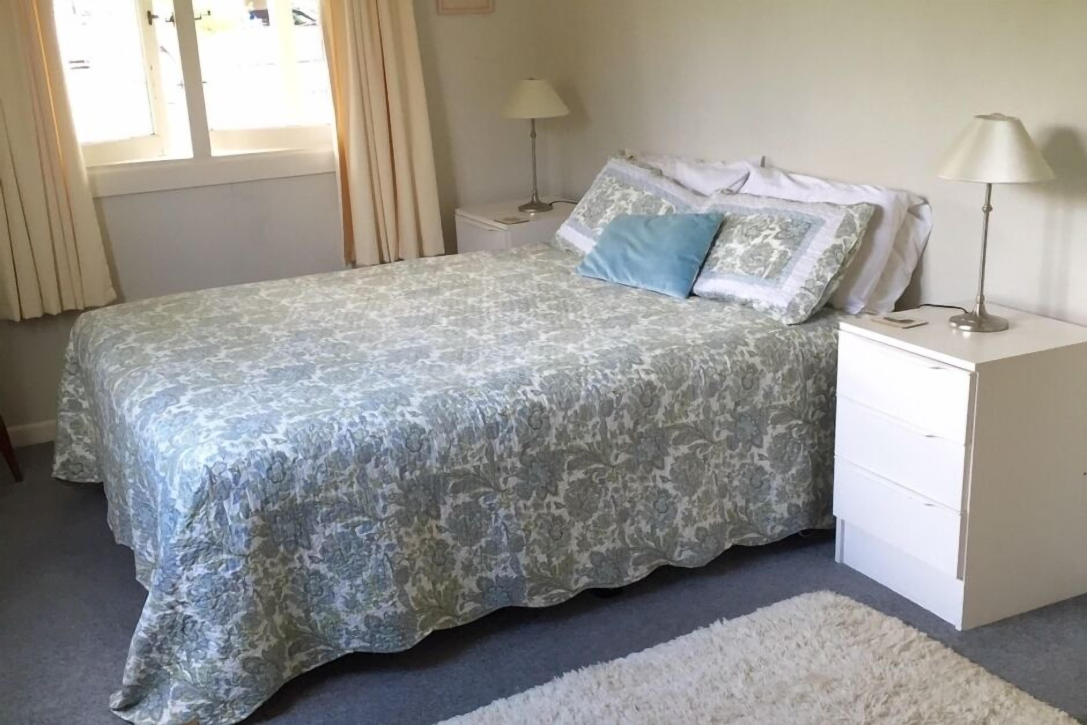 A bedroom with a bed, two bedside tables, and a window with curtains.