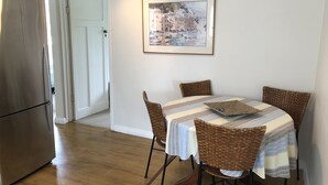 A dining area with a table set for four, surrounded by wicker chairs, a framed picture on the wall, and a stainless steel refrigerator in the background. - Walk to the wharf and village (Mapua (Ruby Bay))