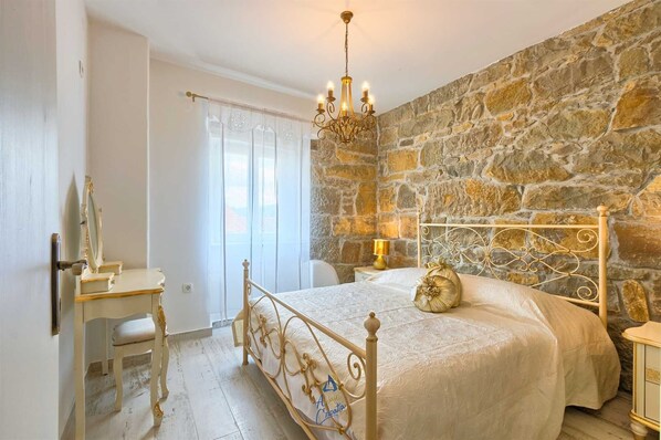 Een slaapkamer met een stenen muur, een kroonluchter, een bed met een decoratief kussen en een bureau met een spiegel.