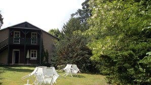Ein zweistöckiges Haus mit Balkon, umgeben von üppiger Bepflanzung und einem Rasen.
