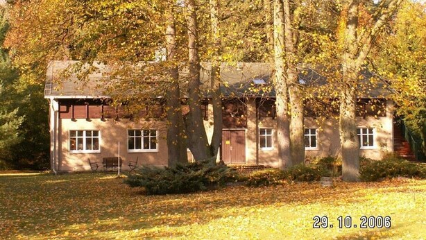 Ein zweistöckiges Gebäude mit geneigtem Dach, umgeben von Bäumen mit Herbstlaub.