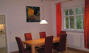 A dining area with a wooden table and red chairs, a painting on the wall, and a window with curtains. - Forsthaus Metzelthin - Holiday with dog (Templin)