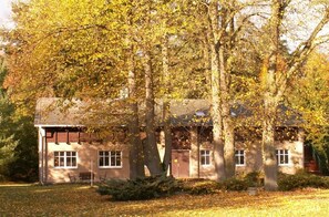 A two-story building with a sloped roof, surrounded by trees with autumn foliage.