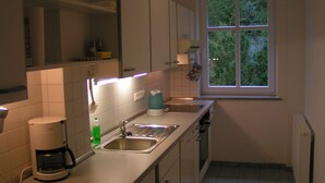 Eine Küche mit weißen Schränken, einer Kaffeemaschine, einem Spülbecken und einem Fenster mit Blick auf Grünflächen.