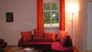Ein gemütliches Wohnzimmer mit einem roten Sofa, einem Glastisch und einem fenster mit Vorhängen.
