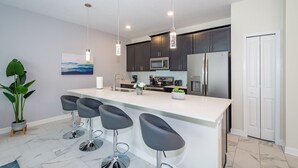 Une cuisine moderne avec des meubles de couleur sombre, des appareils en acier inoxydable et un grand îlot central doté de tabourets de bar.