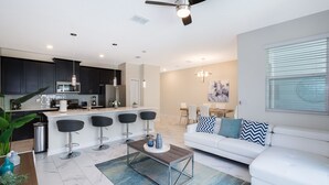 Un espace de vie moderne comprenant une cuisine, un coin repas et un canapé blanc agrémenté de coussins décoratifs.
