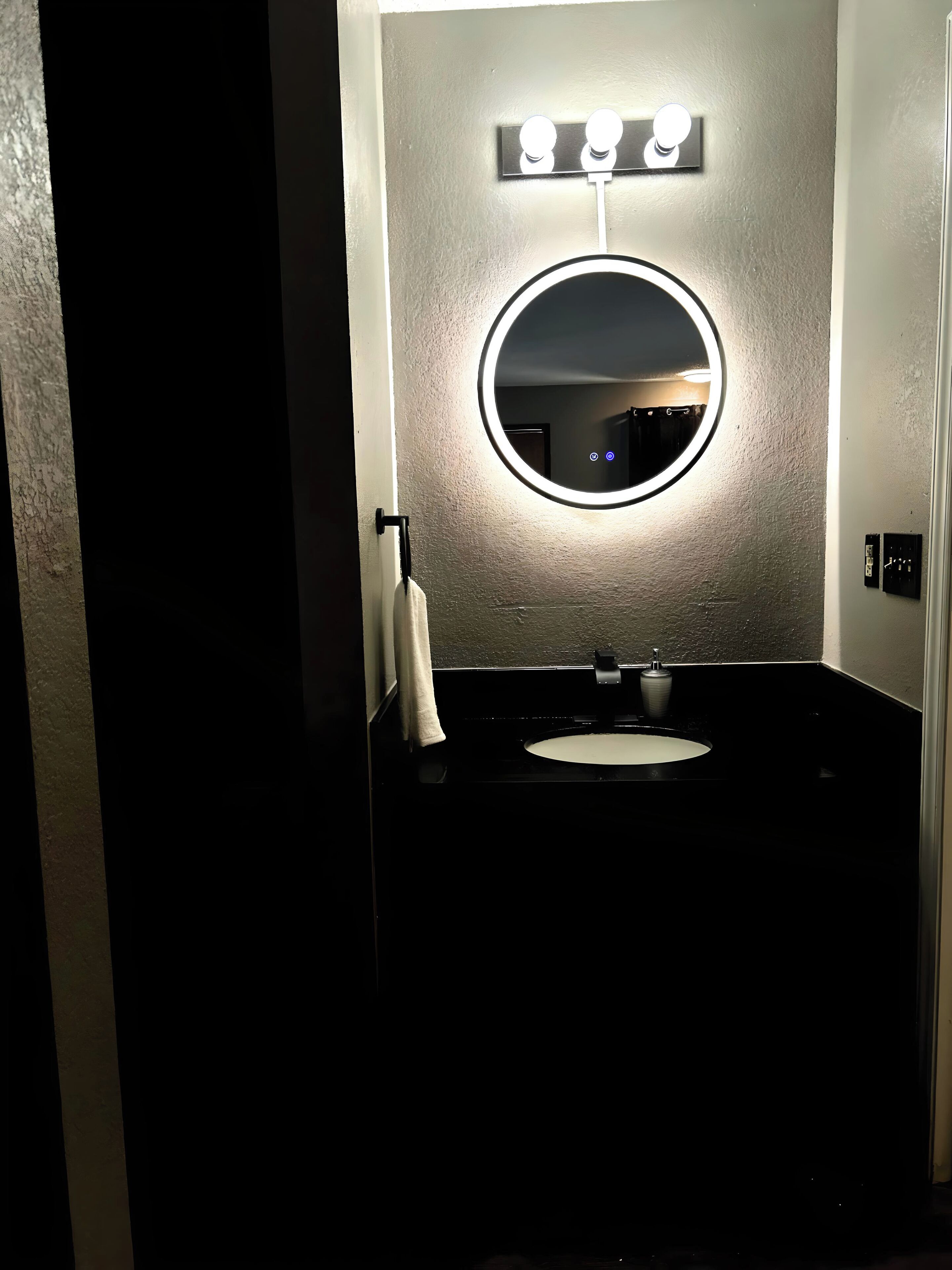 A bathroom with a round mirror, a sink, and a towel rack.