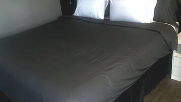 A neatly made bed with a dark grey bedspread and white pillows in a room with a dark headboard and a wooden floor.