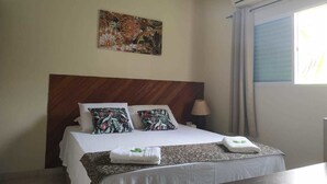 A hotel room with a bed, a headboard, a wall-mounted air conditioner, a window with curtains, and a painting on the wall. - Mares de Camburizinho (São Sebastião)