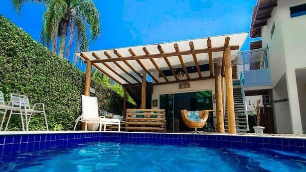 A swimming pool with a wooden pergola, lounge chairs, and a palm tree in the background. - Mares de Camburizinho (São Sebastião)