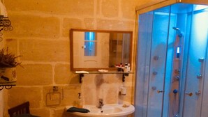 Ein Badezimmer mit Steinwand, Waschbecken, Spiegel, Handtuch und einer Duschkabine.