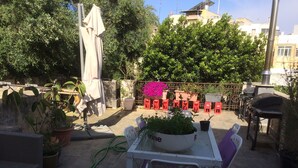 Eine Terrasse im Freien mit Tisch und Stühlen, umgeben von Blumentöpfen und einem Grill.