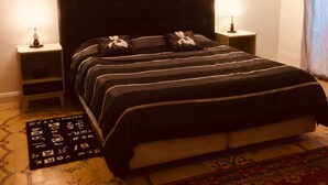 Ein Schlafzimmer mit einem großen Bett, zwei Nachttischen, einem Beistelltisch, einem gemusterten Teppich und einem dekorativen Kopfteil.