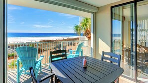 Ein Balkon mit Blick auf den Strand, ein Tisch und zwei Stühle.