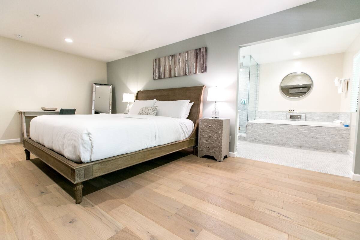 Ein modernes Schlafzimmer mit einem hölzernen Bett, Nachttischen, einem Spiegel und einem Badezimmer mit Dusche und Waschbecken.