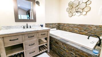 A bathroom with a marble vanity, a large bathtub, and a stone accent wall.