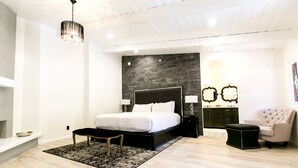 Um quarto moderno com uma cama grande, um banquinho preto, uma chaise longue e uma parede de destaque em pedra.