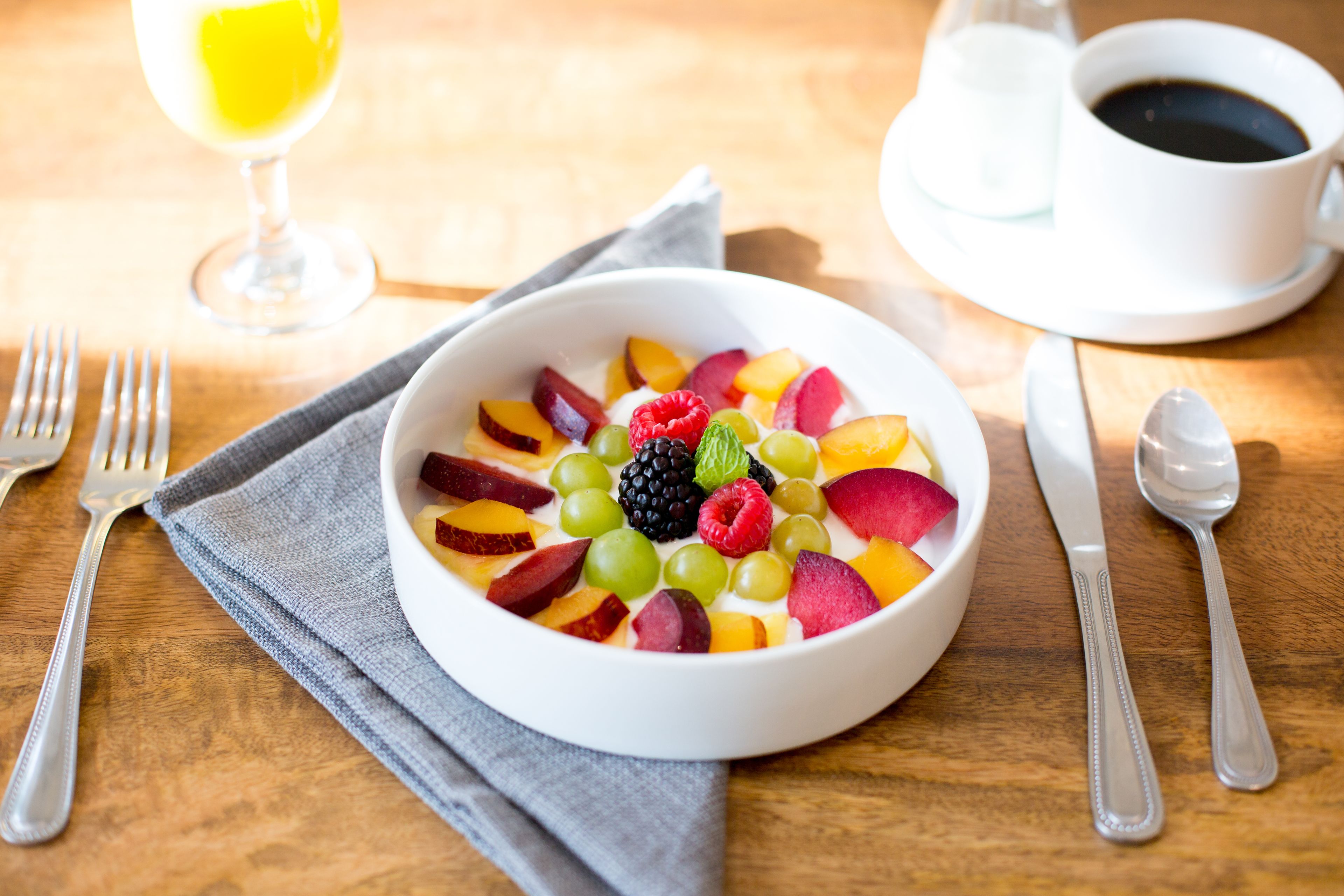Eine Schüssel Obstsalat mit einem Glas Saft und einer Tasse Kaffee auf einem Holztisch.