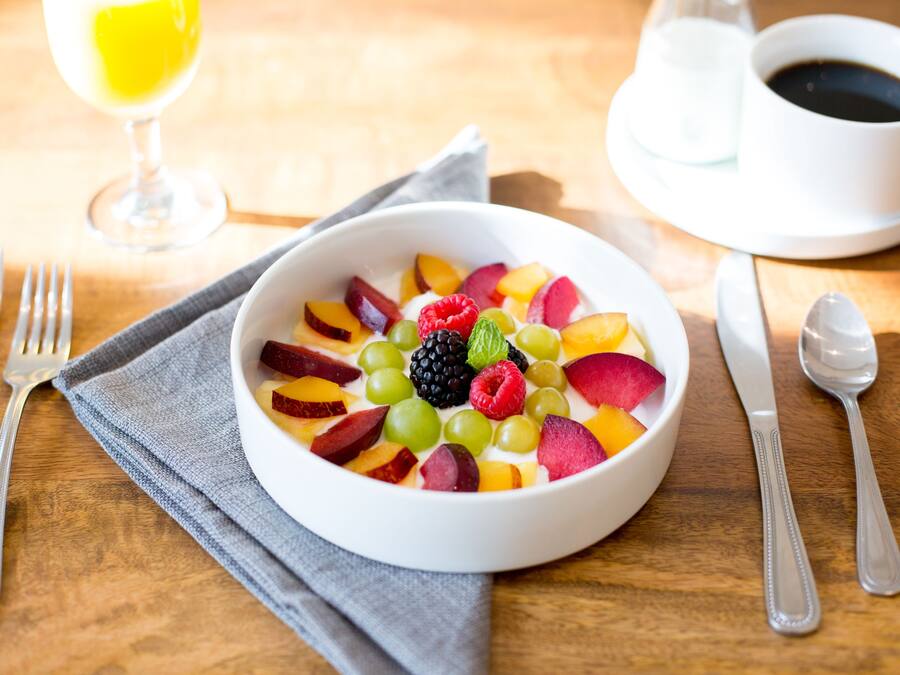 A bowl of fruit salad with a glass of juice and a cup of coffee on a wooden table.