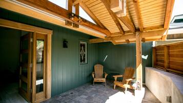 Eine überdachte Terrasse mit Holzbalken, einer grünen Wand und zwei Holzstühlen.