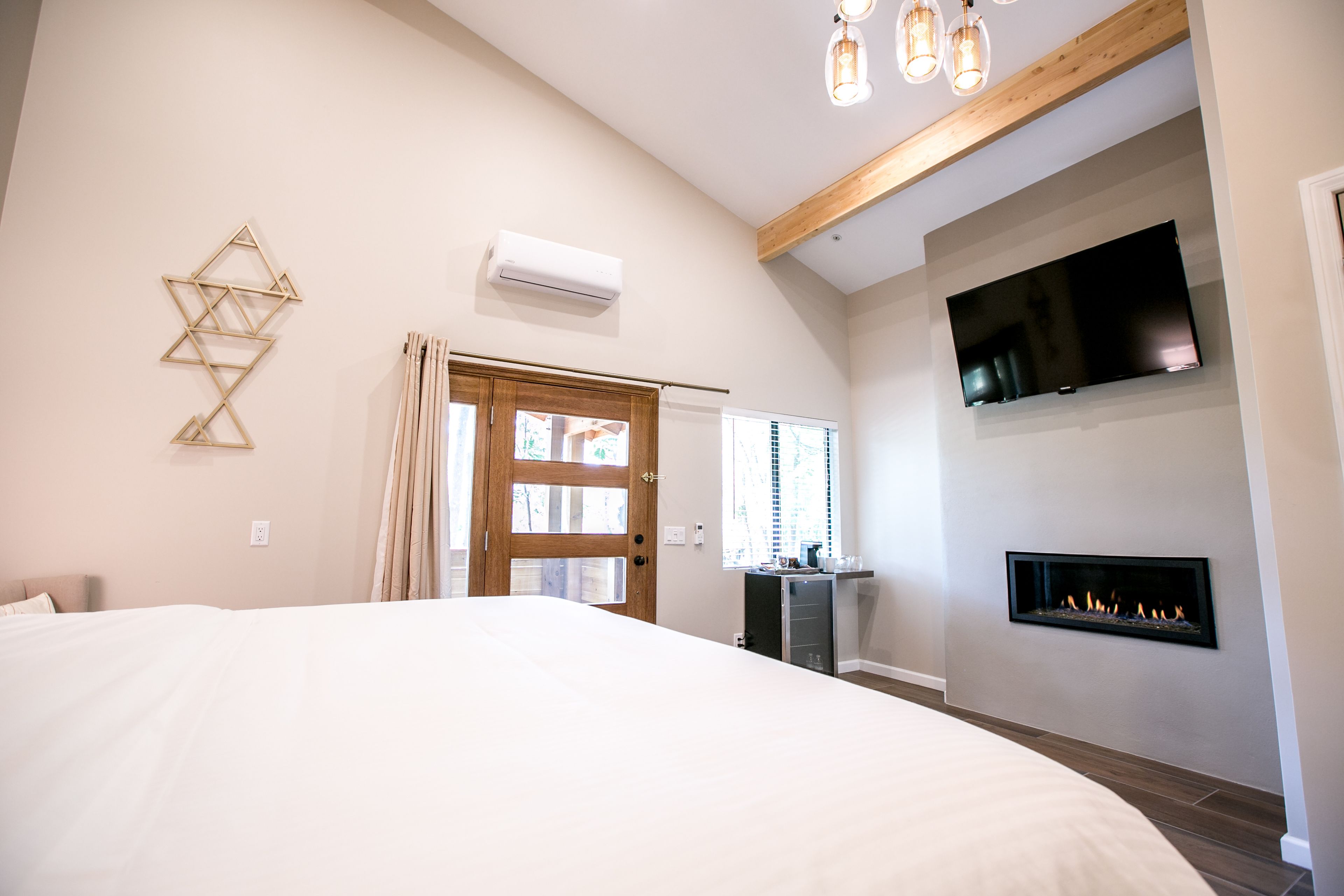 A bedroom with a large bed, a fireplace, a TV mounted on the wall, and a geometric wall decoration.