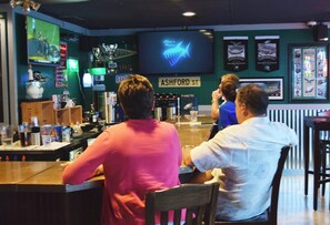 Zona de bar con una pantalla de televisión mostrando un evento deportivo, un cartel que dice