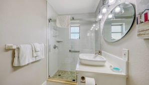 Un baño moderno con cabina de ducha de vidrio, un lavamanos blanco y un espejo grande.