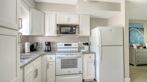 Cocina compacta con muebles blancos, microondas integrado, refrigerador y estufa.