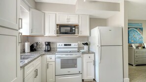 Cocina compacta con muebles blancos, microondas integrado, refrigerador y estufa.
