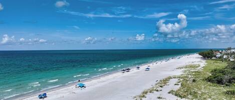 A beach with white sand, clear blue water, and a few umbrellas.