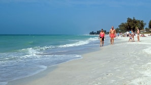 A beach with people walking along the shore, clear skies, and calm sea.