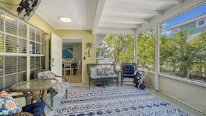 Una sala de estar con ventanales y vista a un jardín tropical, muebles de mimbre y un ventilador de techo.