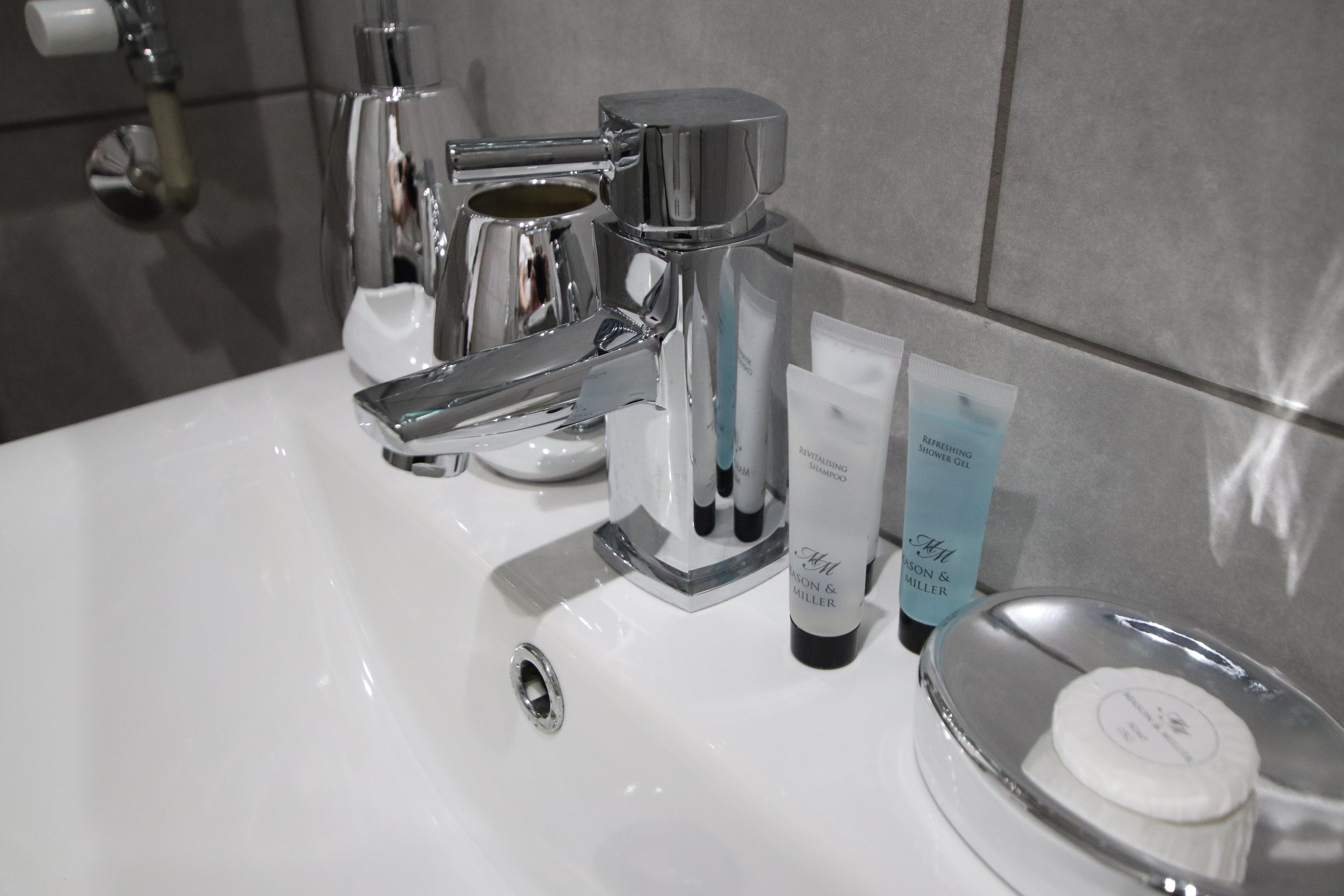 A bathroom sink with a chrome faucet, a soap dispenser, and a bottle of shampoo.