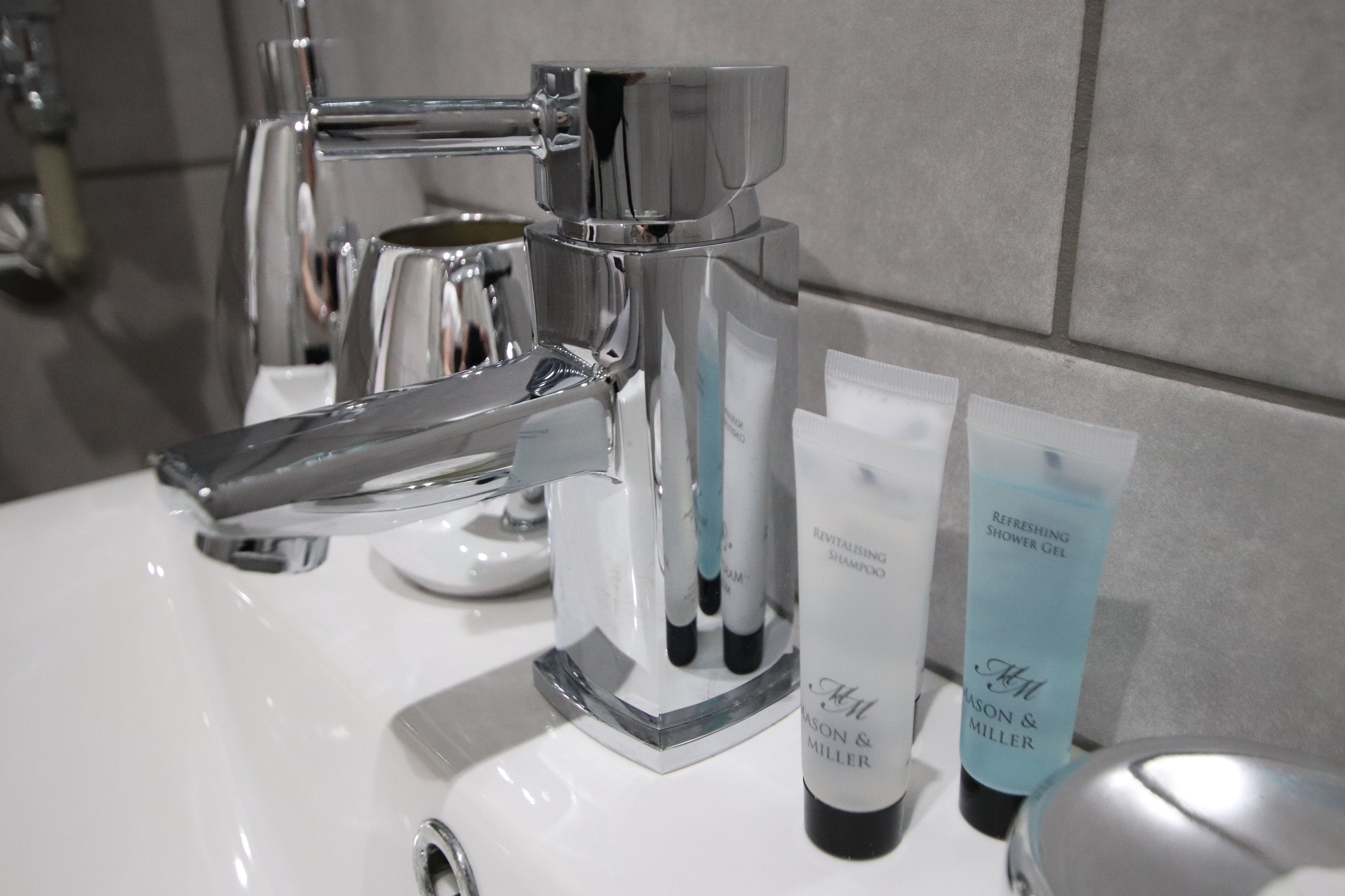 Ein modernes Badezimmer mit chromfarbenem Wasserhahn, einer transparenten Seifenspender und zwei Duschgels.