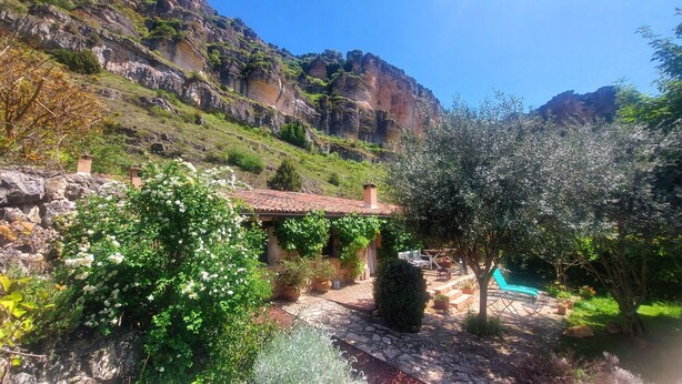 A rustic stone building with a tiled roof, surrounded by lush greenery and a stone pathway.