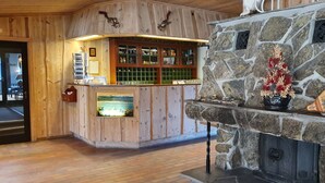 A wooden interior with a stone fireplace, a wooden bar area, and a view of the outside. - Rødungstøl Høyfjellshotell (Al)