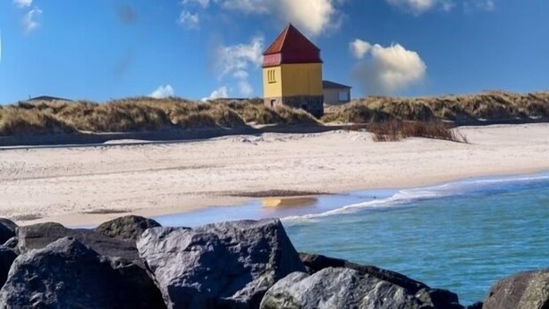 A beach house with a red roof, situated on a sandy beach with dunes in the background. - In the first row to the North Sea (Thyboron)