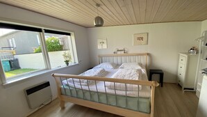 A bedroom with a wooden bed, a window with a view of the outside, a radiator, and a white dresser. - In the first row to the North Sea (Thyboron)