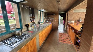 Una cocina con estufa a gas, armarios de madera y una encimera larga. Hay estantes con utensilios de cocina y una ventana con vistas al exterior.