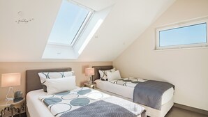 Une chambre avec deux lits, un puits de lumière, une fenêtre et une table de chevet avec une lampe.