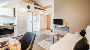 Un appartement moderne comprenant une cuisine, un coin repas et un salon. Il est équipé d’un canapé, d’une télévision et d’une table à manger avec une chaise.