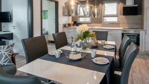 A modern dining area with a table set for four, surrounded by chairs. There are hanging pendant lights above the table, and a vase with flowers on the table. - Design apartment for 3-5 people with south-facing loggia and garden view. Near the lake! (Bensheim)